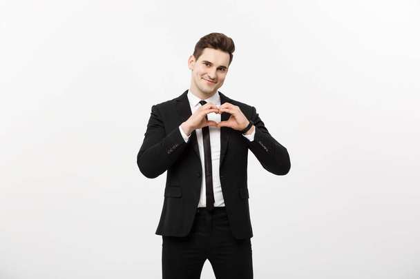 Business Concept: Portrait of charming attractive businessman holding hands in heart gesture and lifting eyebrows while smiling, isolated over white grey background. - Photo, image