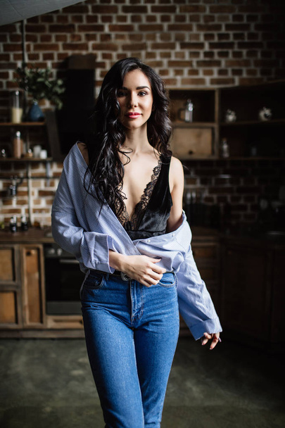 Beautiful brunette in the kitchen, modern housewife, fashion, wooden brown furniture, dressed in blue jeans and a blue shirt - Fotó, kép