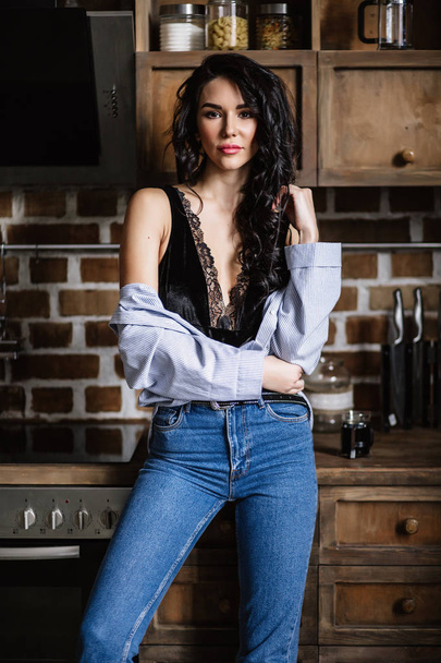 Beautiful brunette in the kitchen, modern housewife, fashion, wooden brown furniture, dressed in blue jeans and a blue shirt - Foto, imagen
