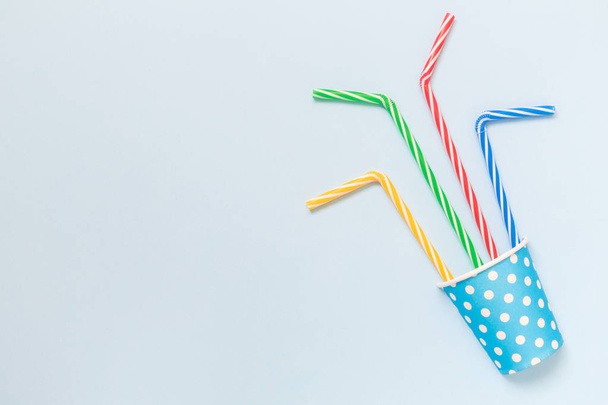 Copa de papel con pajitas de beber multicolores aislados en el concepto minimalista azul
. - Foto, Imagen
