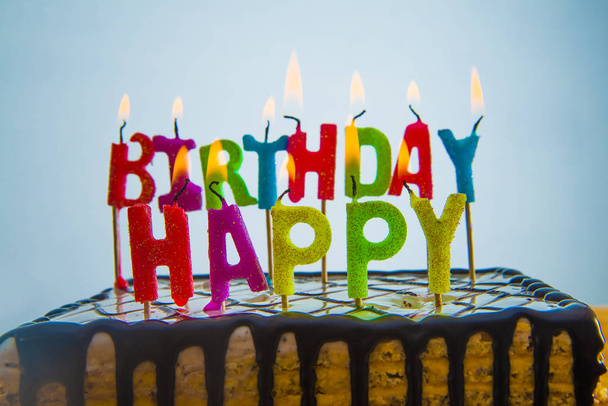 pastel de cumpleaños marrón chocolate con velas quemadas de colores - palabras hechas de letras feliz cumpleaños
  - Foto, Imagen