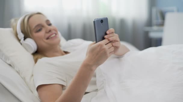 Morning in bed, teenager girl wearing headphones and communicating in network - Imágenes, Vídeo