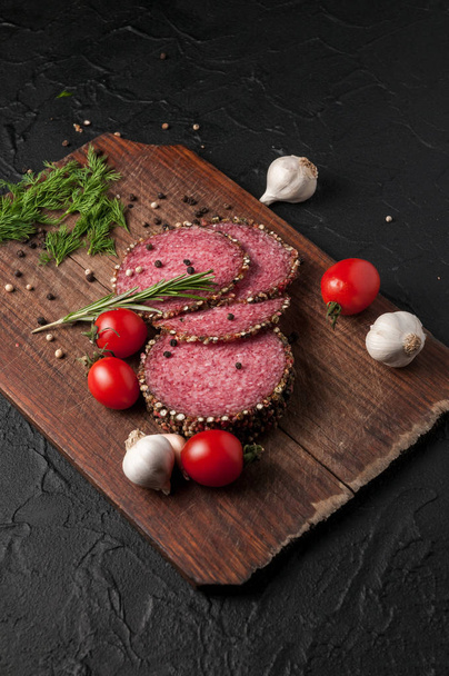 Smoked salami on a black table and a brown board. Sausages with  - Foto, imagen