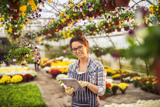 beautiful young female professional gardener using tablet pc in modern greenhouse  - Valokuva, kuva