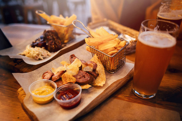delicious smoked sausage with chips, french fries and steak with sauce on wooden board.  - Photo, Image