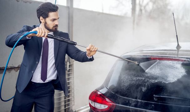 szép elegáns fiatal szakállas férfi öltöny autó mosás: a kézi autómosó önkiszolgáló station - Fotó, kép