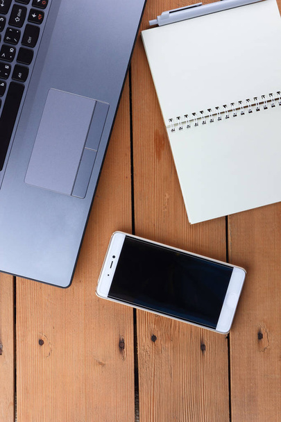 Laptop op een houten achtergrond, een baan op een oude tafel, smartphone en laptop, pen en glazen op de werkplek, kopie ruimte, kantoorruimte in een minimalistische stijl - Foto, afbeelding