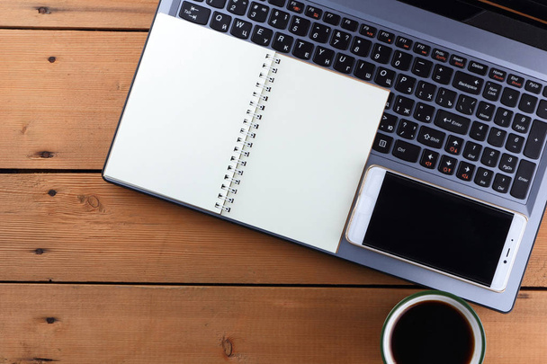 Laptop en kopje koffie op een houten achtergrond, werkstation in een oud Bureau, smartphone en een notebook, pen en glazen op de werkplek, ontwerper werkstation, kunst - Foto, afbeelding