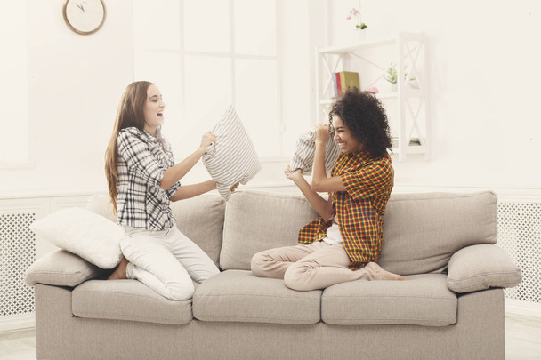 Deux jeunes femmes ayant une bataille d'oreillers sur le canapé
 - Photo, image