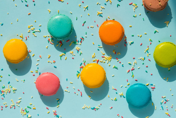 Top view of scattered colorful macaroons and sugar sprinkles over blue background. Abstract food background. - Valokuva, kuva