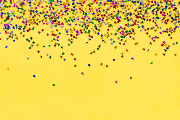 Разбросанные в форме звезды красочные блестящие конфетти на желтом фоне. Копирование пространства
. - Фото, изображение