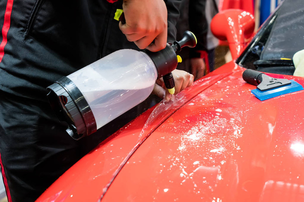 İşçi boya koruması filmi yüklemek için arabaya su sıkıyor - Fotoğraf, Görsel