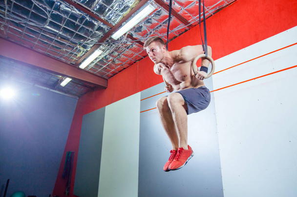 Muscle-up exercise young man doing intense cross fit workout at the gym on gymnastic rings. - Фото, изображение
