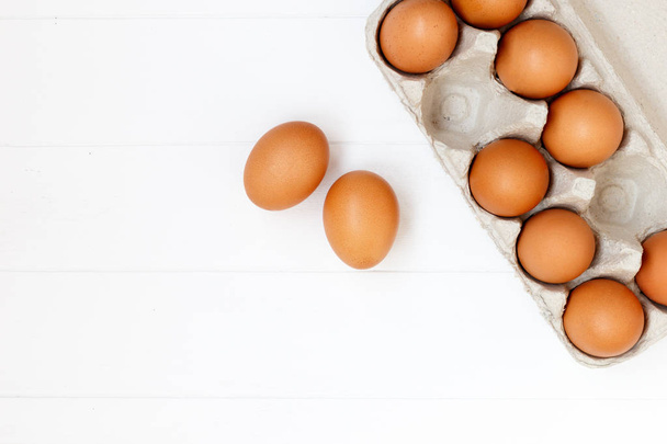 свежие или сырые коричневые яйца на белом деревянном фоне, вид сверху, фл
 - Фото, изображение