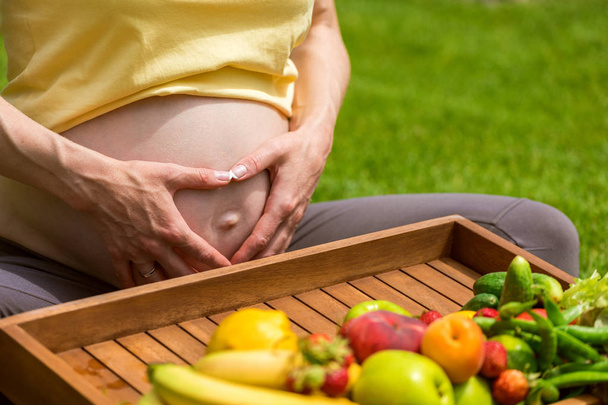 Pregnant woman sitting on grass and holding an apple in hand - Фото, изображение