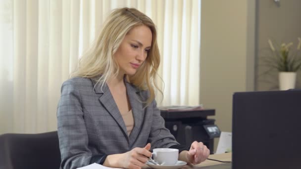 Bella donna d'affari in giacca e cravatta lavora con tazza di caffè sul posto di lavoro
. - Filmati, video