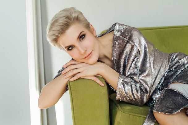 schöne blonde Frau mit kurzen Haaren sitzt auf grünem Sofa - Foto, Bild
