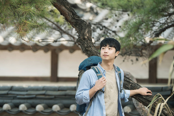 Ένας νεαρός άνδρας που κάνει ένα backpacking ταξίδι σε μια κορεατική παραδοσιακή κατοικία. - Φωτογραφία, εικόνα