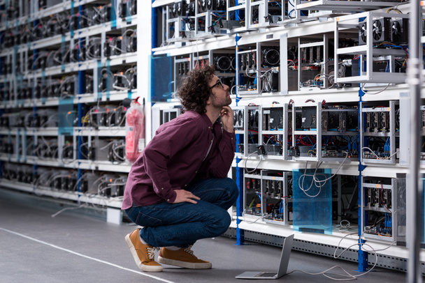 young computer engineer sitting on floor and looking at cryptocurrency mining farm - Φωτογραφία, εικόνα