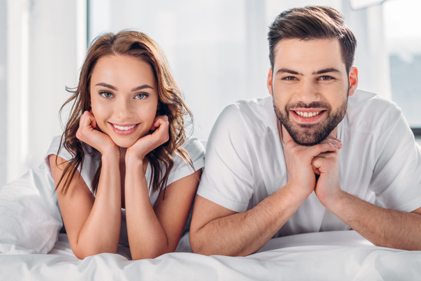 portrait of smiling couple looking at camera while resting on bed together - Foto, Bild