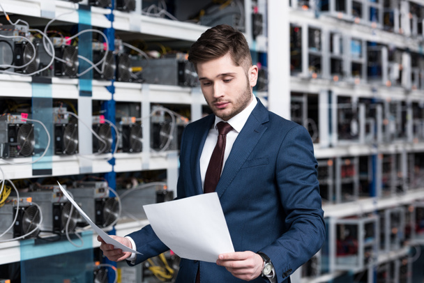 handsome young businessman reading business documents at cryptocurrency mining farm - Foto, Imagen