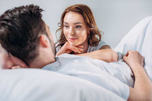 young pretty woman leaning on boyfriend while resting on bed together isolated on grey - Photo, Image