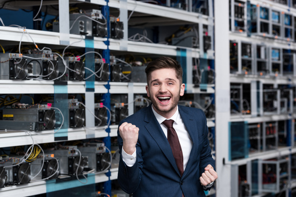 happy young businessman celebrating victory and raising fist at cryptocurrency mining farm - Photo, Image