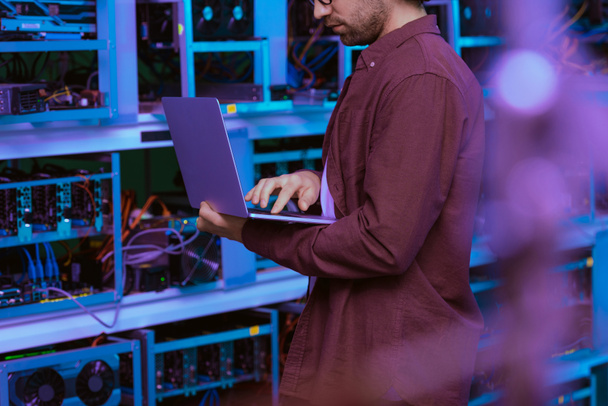 обрізаний знімок молодого комп'ютерного інженера, що працює з ноутбуком на гірничодобувній фермі Ethereum
 - Фото, зображення