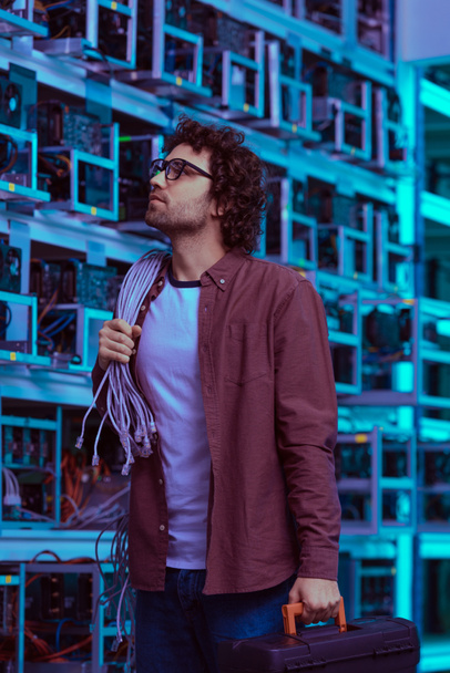 young computer engineer with wires on shoulder at ethereum mining farm - Photo, Image