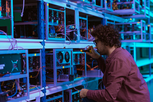 Junger Computeringenieur repariert auf Kryptowährungsfarm mit Schraubendreher - Foto, Bild
