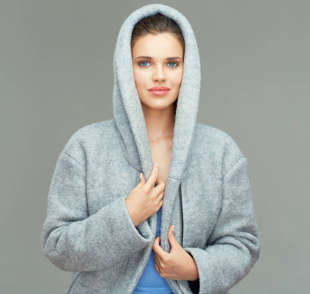 young woman wearing coat and touching collar of hood while posing on gray background - Φωτογραφία, εικόνα