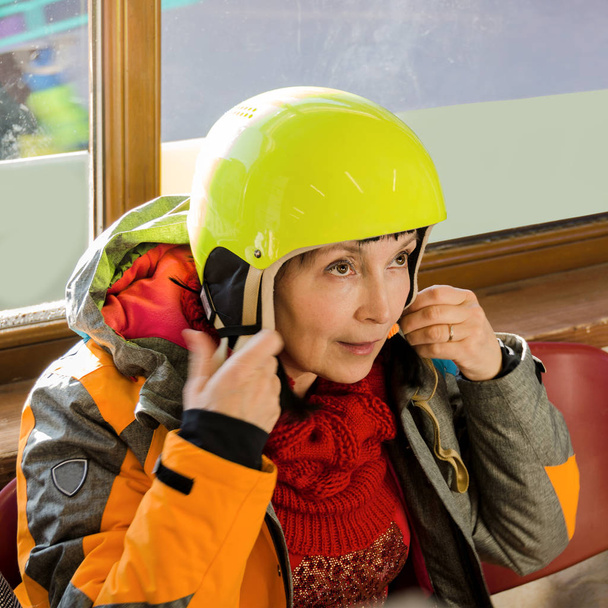 Una mujer con una chaqueta de invierno se pone un casco en la cabeza. Cuadrado
. - Foto, imagen