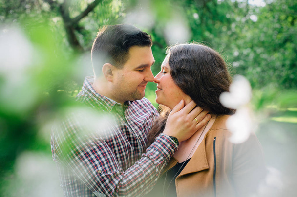 Jonge stijlvolle gelukkige paar verliefd knuffelen in de bloeiende tuin. Man en vrouw hebben romantische datum buitenshuis. - Foto, afbeelding