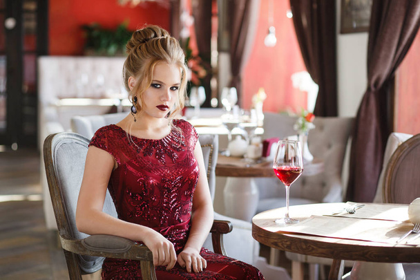 Elegant lady with glass of red wine in restaurant. Seductive young woman looking to camera - Fotografie, Obrázek