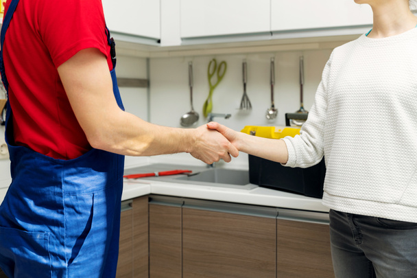 plumber and woman shaking hands after repairs at home kitchen - Photo, image