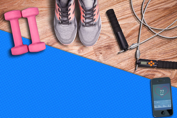Trénink v tělocvičně modrá podložka fitness Svatodušní-švihadlo. Posilovna a vybavení na trénink na pozadí dřevěné podlahy. Běžecké boty a cvičení. Stopwach Svatodušní srdeční frekvence na smartphone. - Fotografie, Obrázek