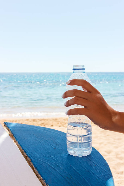 Mano femminile che tiene una bottiglia d'acqua sulla spiaggia, fondo mare
 - Foto, immagini