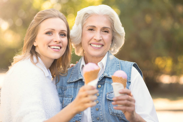 古い母親屋外でアイスクリームを楽しんで幸せな若い女 - 写真・画像