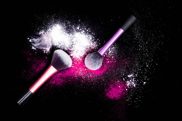 Πινέλα Μακιγιάζ με πολύχρωμα σκόνη χυθεί glitter σκόνη σε μαύρο φόντο. Μακιγιάζ βούρτσα στο πάρτι της Πρωτοχρονιάς με φωτεινά χρώματα. Λευκό και ροζ σκόνη. - Φωτογραφία, εικόνα