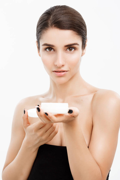 Beauty Youth Skin Care Concept - Close up Beautiful Caucasian Woman Face Portrait presenta tarro de crema para el cuidado de la piel sobre fondo blanco
. - Foto, imagen