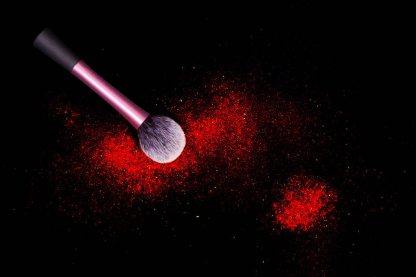 Brush with red powder spilled glitter dust on black background. Red powder on black table. - Photo, Image