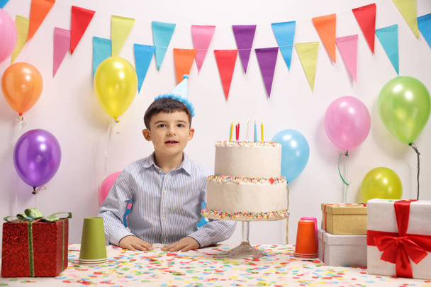 A kisfiú egy csapat kalap és egy születésnapi torta dekoráció zászlókkal és léggömbök a falhoz - Fotó, kép