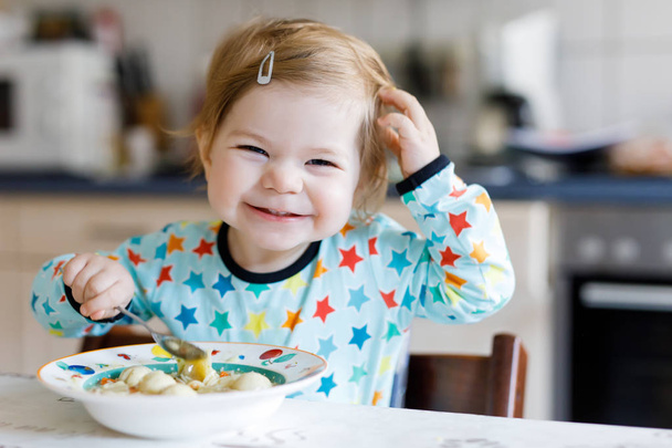 Очаровательная малышка ест с ложки овощного супа с лапшой. продовольствие, дети, питание и люди концепция
 - Фото, изображение