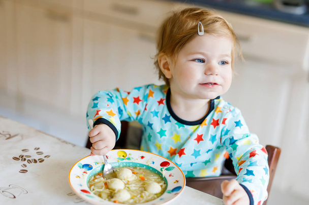 Очаровательная малышка ест с ложки овощного супа с лапшой. продовольствие, дети, питание и люди концепция
 - Фото, изображение