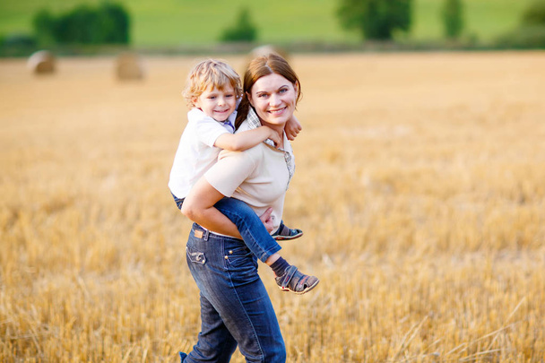 夏の麦畑に腕に子供男の子を持つお母さん - 写真・画像