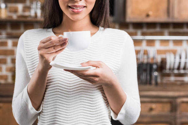 cropped shot of smiling african american woman holding white coffee cup and saucer - Foto, Imagen