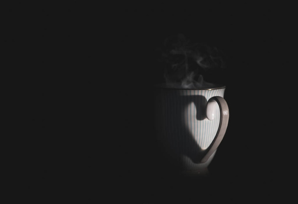 Une tasse de thé chaud dans le noir (mise au point sélective sur la poignée
) - Photo, image