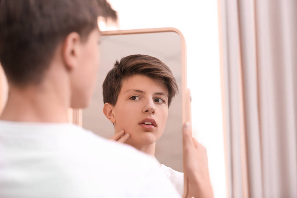 Teenage boy with acne problem looking in mirror at home - Foto, afbeelding