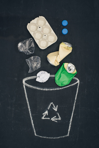 different types of trash falling into drawn trash bin with recycle sign on chalkboard - Photo, Image