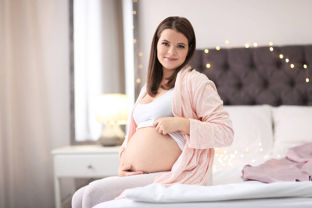 美しい妊娠中の女性座っていますベッドに家 - 写真・画像